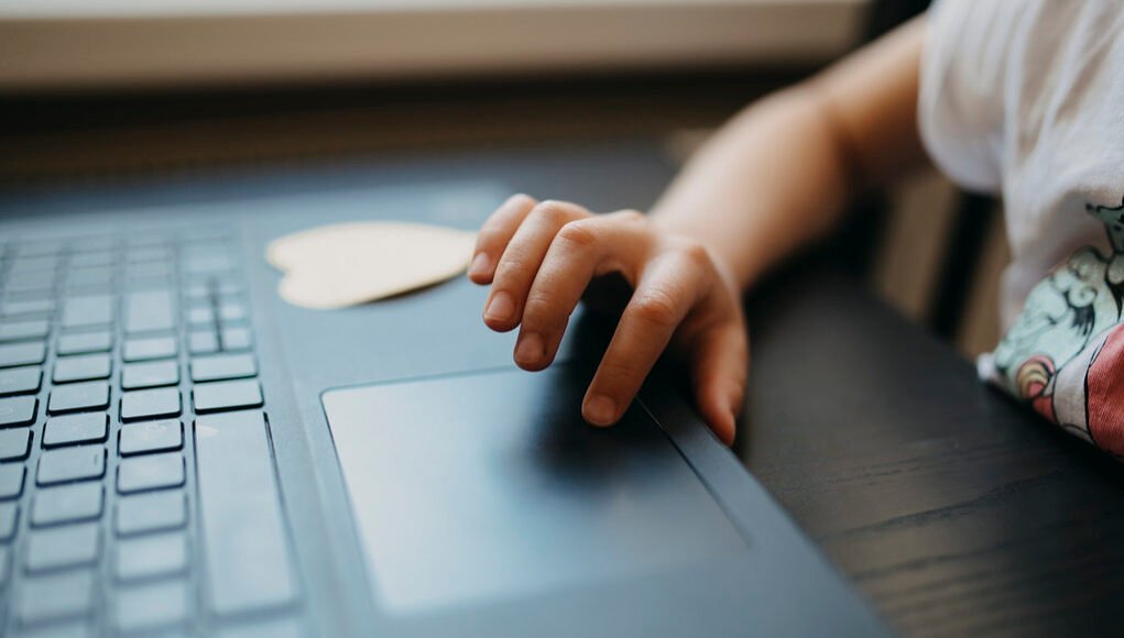 Child interacting with a laptop touchpad while sitting at a table