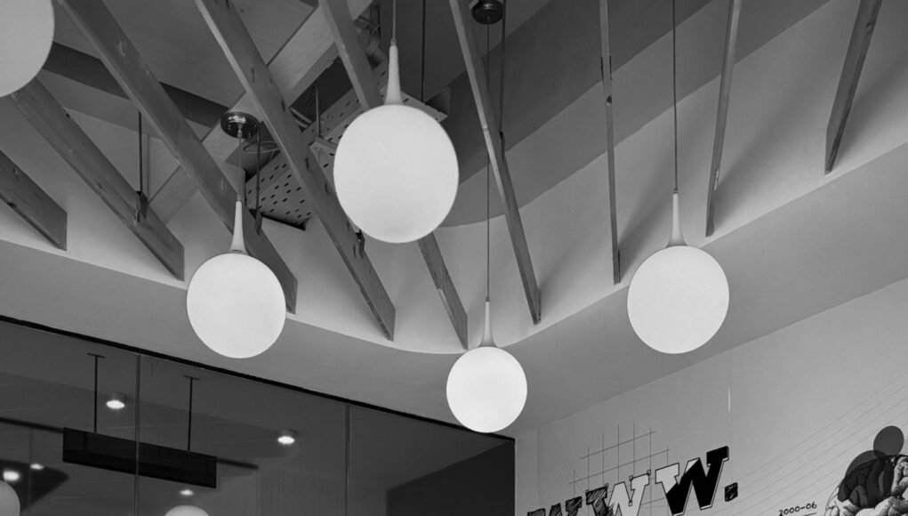 Minimalist workspace with a large screen, tripods, web design graphics, and pendant lights.